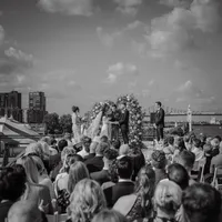 Cérémonie de mariage au Belvédère du Vieux-Port de Montréal, couple sous arche florale avec invités et skyline en arrière-plan, portrait en noir et blanc