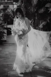 Mariée souriante tenant son bouquet, robe de dentelle à traîne fluide, devant un décor de plantes tropicales à Aquatopia, Ottawa, portrait en noir et blanc