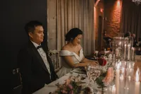 Mariés souriants à la table d'honneur, robe bustier blanche et smoking noir, décor floral et chandelles, ambiance chaleureuse à la Gare Viger, Montréal