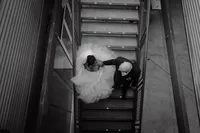 Vue en plongée des mariés se tenant la main dans un escalier métallique, robe volumineuse et complet sombre, moment tendre au Belvédère du Centre des Sciences, Montréal