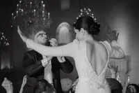 Mariée en robe dos nu perlée dansant avec un invité, chandeliers et miroir orné en arrière-plan, ambiance festive à la Maison Principale