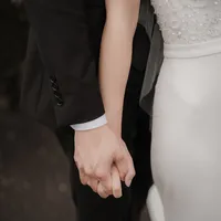 Mains enlacées d'un couple marié, détail de la robe blanche et du costume noir