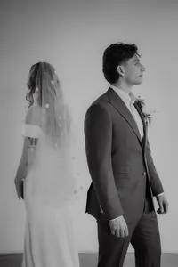 Mariés dos à dos sur fond neutre, voile fleuri translucide et boutonnière florale, portrait épuré en studio au Studio Giovanelli