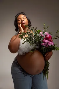 Woman posing with baby bump and a bundle of flowers.