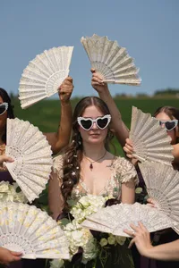 Edgy tattoo pierced Alternative Bride surrounded by fans photography trend in lush green field backdrop bridesmaids with fans surrounding her face wearing heart shaped sunglasses