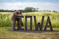 Engagement photoshoot with midwest couple at center grove orchard at the Iowa sign in front of a lush corn field