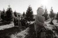 A family sits in the grass amongst the balsam trees for photos. One of the daughters runs towards the camera while the family smiles in the background.