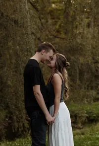 Engaged couple standing forehead to forehead under a willow tree during a romantic Maine engagement photography session
