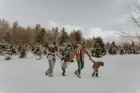 Family of five walking through a tree farm in Maine during a winter family photoshoot, cozy and candid New England family photography capturing joyful outdoor moments.