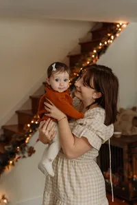 A mother cradles her baby while wearing a red dress in a New England home. Fine art lifestyle family photography capturing tender, intimate, and heartfelt parent-child moments.