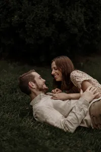 A couple rolls together in the grass, cozy and laughing during their engagement photoshoot in New England. Fine art lifestyle photography capturing romantic, intimate, and playful moments.