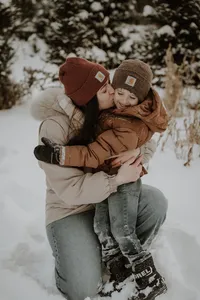 A mother snuggles her young son in the snow during a New England winter. Fine art lifestyle family photography by Damini Photography capturing warmth in the winter.