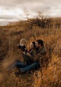 Parents playing with their toddler in a grassy field in New England. Fine art lifestyle family photography capturing joyful, candid moments.