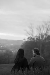 A couple sits together in the grass, cozy and calm during their engagement photoshoot in New England. Fine art lifestyle photography capturing romantic, and intimate photos.