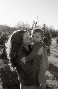 A mother holds her baby daughter and kisses her on the cheek during a family photoshoot in New England.