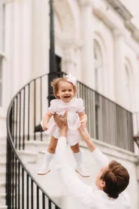 Charleston Baby Milestone Photographer - Toddler gets tossed into the air by her father during Baby Milestone Portraits in downtown Charleston, SC
