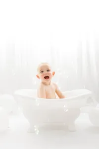 Baby smiles at the camera while sitting in a miniature claw foot splash bath tub during his first birthday Cake Smash Photoshoot at Holy City Babies Portrait Studio in Charleston, SC.