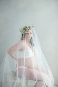 Pregnant woman with floral crown and veil draped over her body by by Suzanne Karp Photography