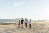 Family portrait outside in a dry field during a golden hour, all holding hands and smiling at each other by Suzanne Karp Photography in San Francisco California
