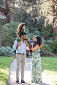 Family photo of dad with daughter up on his shoulders and mom holding toddler while they all walk outside eon a park path by Suzanne Karp Photography in Marin County California