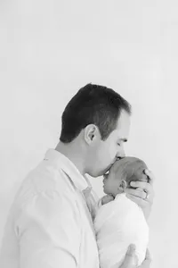 Father kissing the forehead of newborn baby in black and white by Suzanne Karp Photography in Wine County California