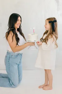 Image of mother holding a birthday cake with candle in front of the daughter like a surprise by Suzanne Karp Photography in San Francisco California