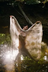 Woman standing in shallow water with sheer fabric during an outdoor film boudoir session.