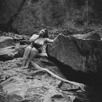 Woman posed among rocks beside a creek in a black-and-white outdoor boudoir portrait.