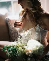 Woman in white lace lingerie holding flowers in soft window light during a film boudoir session.