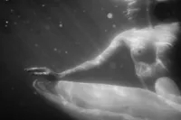 Black-and-white underwater portrait of a woman partially submerged, with flowing fabric and light rippling across her body.
