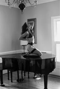 Woman in lingerie kneeling on a grand piano during a black-and-white boudoir session.