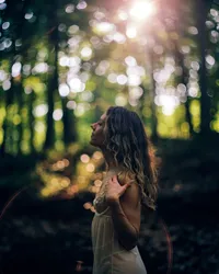 Woman in a sheer dress standing in sunlit woods during an outdoor film boudoir session
