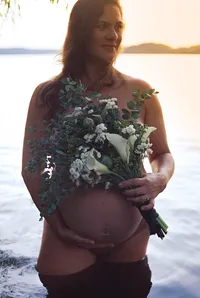 Pregnant woman holding a floral bouquet beside the water during a sunset maternity portrait.