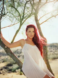 Red-haired woman in a sheer white slip standing between tree branches in bright desert sunlight.