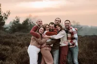 Familie geeft elkaar een grote groepsknuffel met de ondergaande zon op de achtergrond tijdens een familieshoot