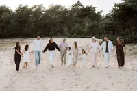 Familie wandelt hand in hand lachend over het zand tijdens de ondergaande zon met een familieshoot