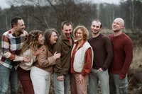 Kinderen kijken lachend naar hun ouders terwijl ze op een rij staan tijdens een fotoshoot met de familie in de omgeving Apeldoorn