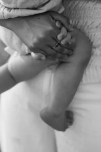zwart wit beeld van een detail foto van moeders hand die dochters hand vasthoudt en het beentje van haar baby