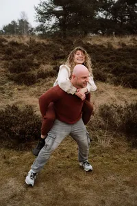 Zus zit bij broer op de rug tijdens een fotoshoot met de familie in de omgeving Apeldoorn