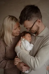 Vader draagt baby op zn borst en moeder kruipt dicht tegen hen aan tijdens een newbornshoot in de omgeving van Apeldoorn
