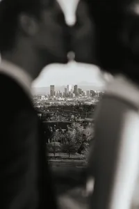 A slightly blurred image of a couple kissing with a city skyline in focus behind them.
