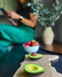 Avocado halves and strawberries as a healthy fats nutrition snack, with a dietitian on her phone in the background