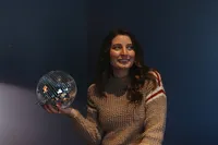 A woman in a sweater holds a disco ball, subtly smiling, symbolizing corporate event planning creativity in Northwest Arkansas.