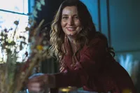 A smiling woman with long brown hair arranges flowers indoors, reflecting her expertise as a luxury event planner in Northwest Arkansas.
