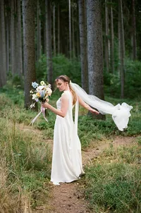 Ethereal bride in a flowing wedding dress posing in a dreamy pine forest, captured on film.