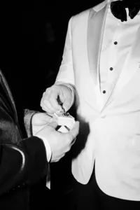 Candid shot of a groom in a stylish white tuxedo receiving wedding rings from the best man during the ceremony.