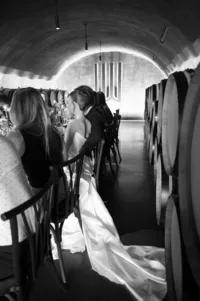 Bride seated during an intimate rehearsal dinner in a winery cellar surrounded by candlelight and guests.