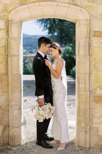 Bride and groom standing beneath Sunstone Winery stone arch during romantic vineyard wedding