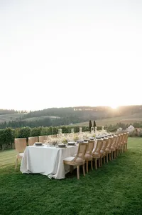 Elegant reception table styled with wooden chairs and organic linen, overlooking rolling vineyard hills at sunset.
