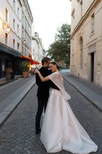 Bride and groom standing together in the middle of a Paris street surrounded by historic architecture and glowing evening lights.